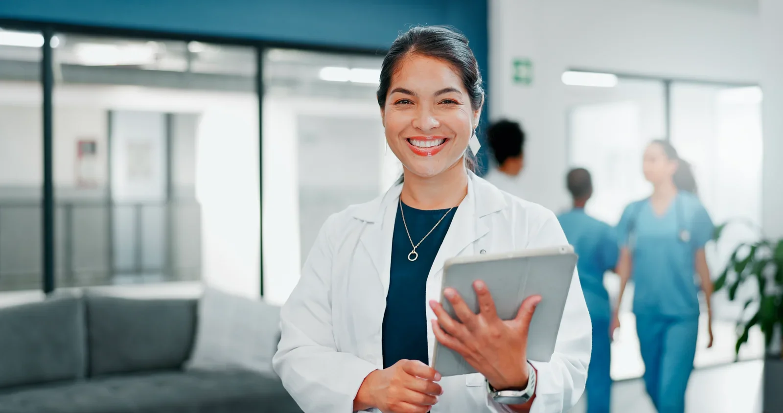 Praticienne en blouse blanche avec une tablette, dans le couloir d'une clinique
